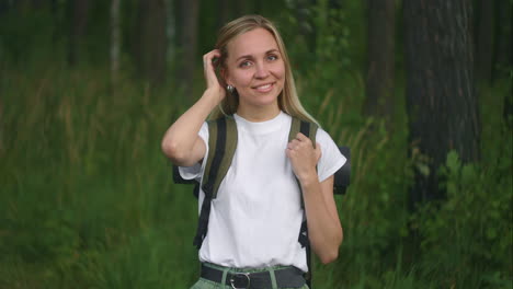 Portrait-of-a-young-woman-traveler-in-the-sun-looking-directly-into-the-camera-and-smiling-flirting-Traveler-with-a-backpack-in-the-Park-and-in-the-woods-in-slow-motion